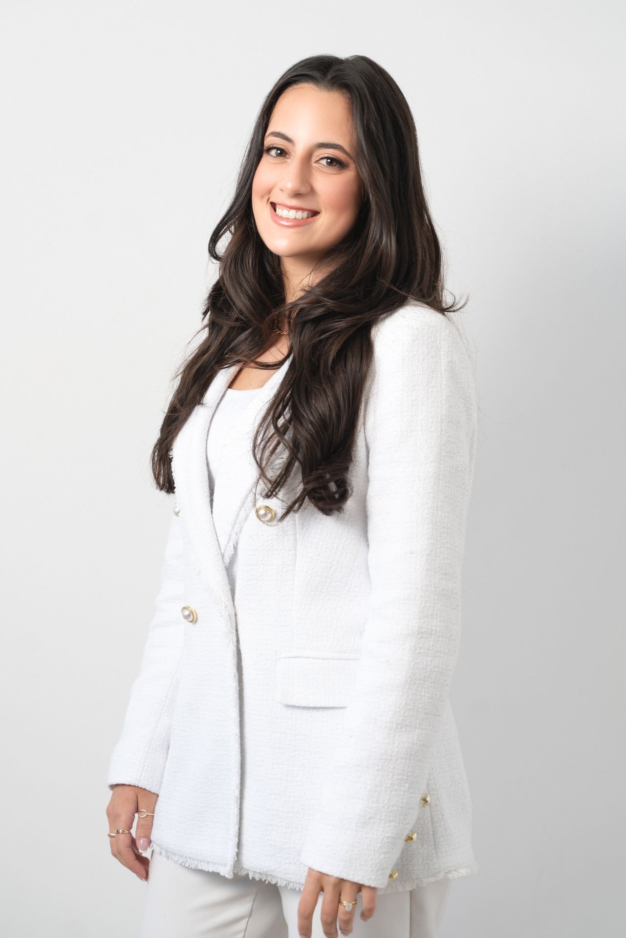 Person wearing a white textured blazer with gold buttons and long dark hair.